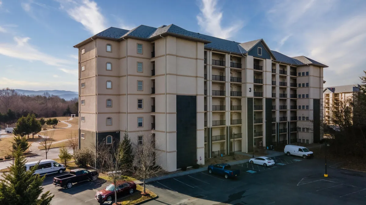 This image depicts the building's welcoming facade, a spacious parking lot, and surrounding greenery. The scene conveys a sense of arrival and highlights the accessibility of the property within a friendly and communal environment.