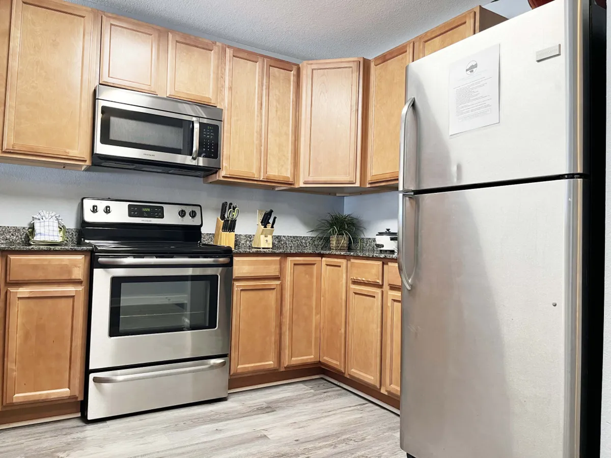 A warm, inviting kitchen featuring stainless steel appliances, granite countertops, wooden cabinets, and an array of kitchen utensils. The modern setup is clean and functional, with everything needed for cooking up both quick snacks and elaborate meals.