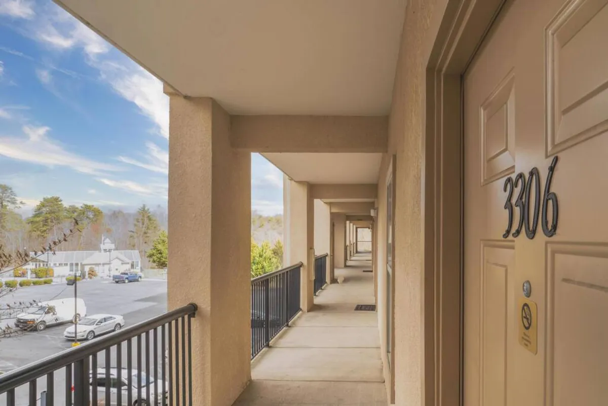 The image shows the exterior view of the condo, with the door number 3306 and a balcony railing in the foreground. In the background, distant trees and buildings are visible, evoking a sense of connection to the outdoors and the surrounding mountain setting.
