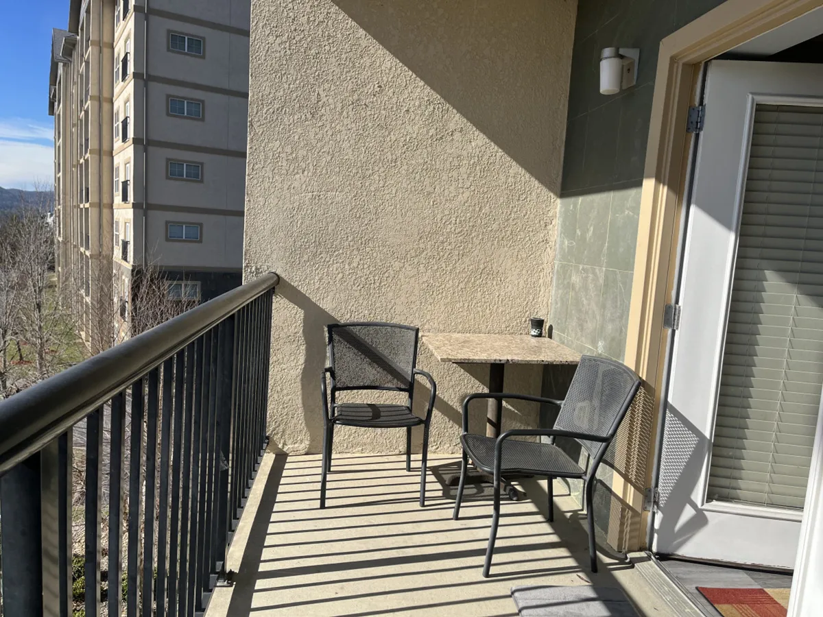 The image shows two black chairs and a small table on the balcony, with a tranquil view of the outdoors. This setting suggests peaceful moments spent enjoying the fresh air after a day of exploring nearby attractions.