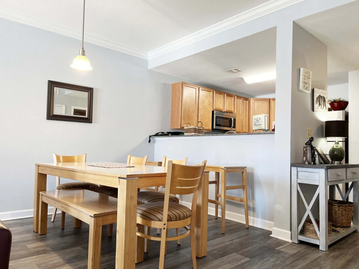 A welcoming dining area with a table set adjacent to the kitchen counter, under a stylish pendant light. The arrangement encourages group meals and gatherings, with a mirror reflecting the cozy setting.