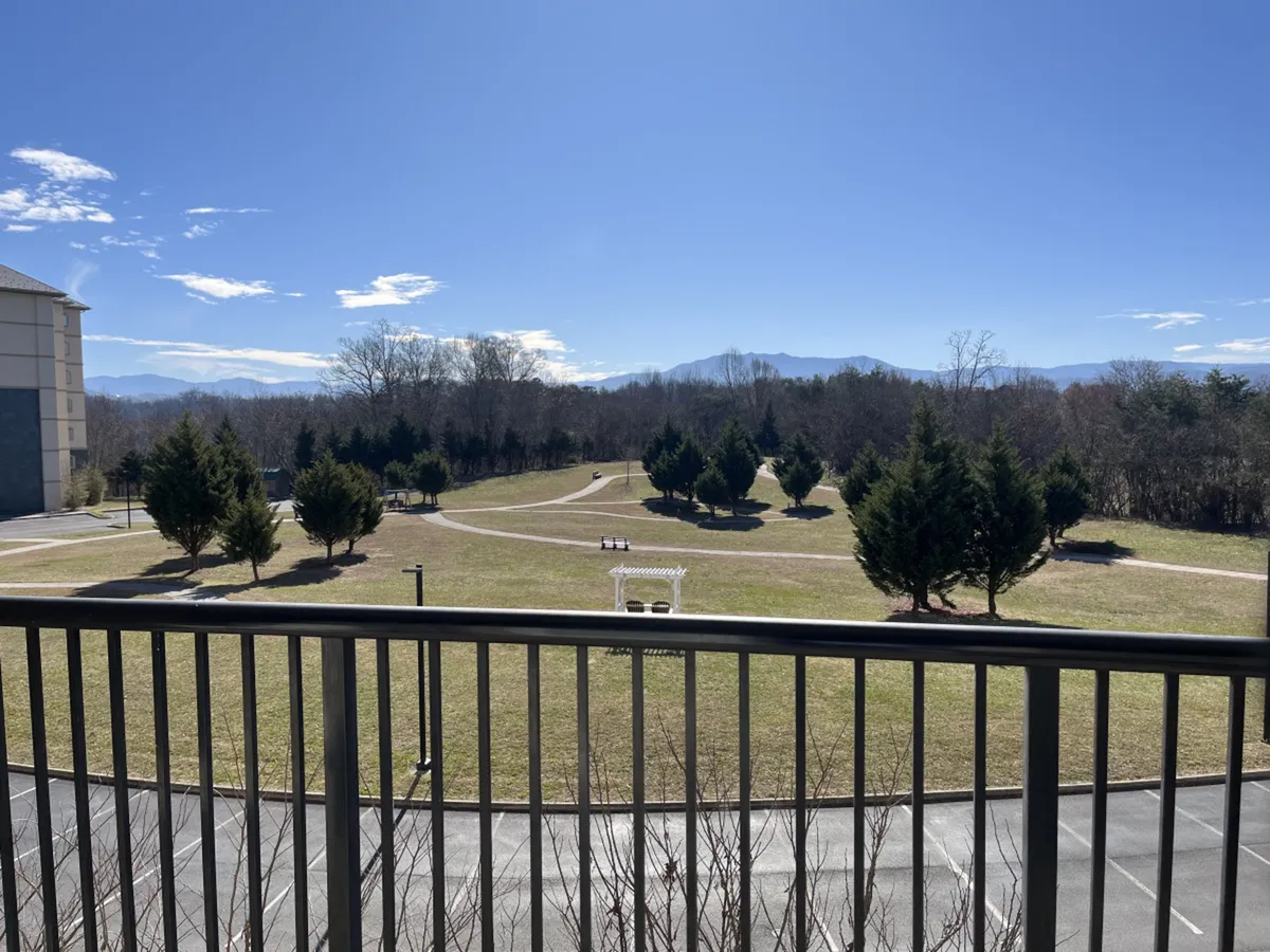 A wide view of the grounds, showcasing lush green lawns, meandering pathways, a gazebo, and mountains in the distance. The space is open and tranquil, perfect for kids to run and play, families to picnic, and guests to gather for outdoor activities against a natural mountain backdrop.